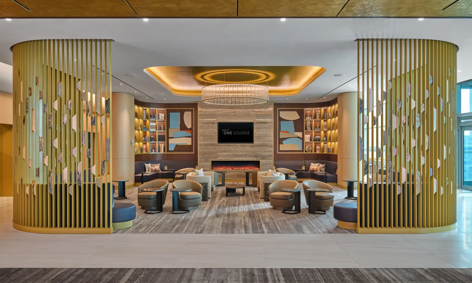Tan leather seating around a linear fireplace under a circular chandelier in the Delta One Lounge at New York JFK Terminal 4.