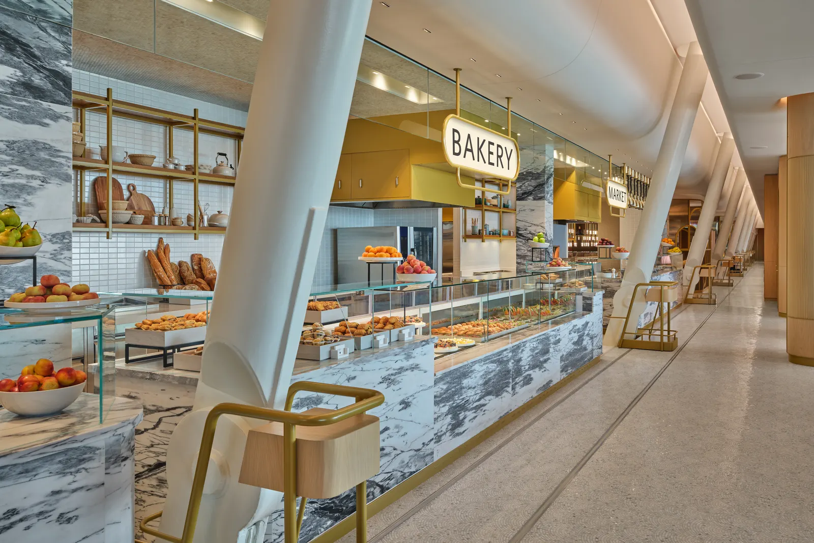 Bakery and Market walk-up counters with marble displays under yellow signs in the Delta One Lounge at New York JFK Terminal 4.