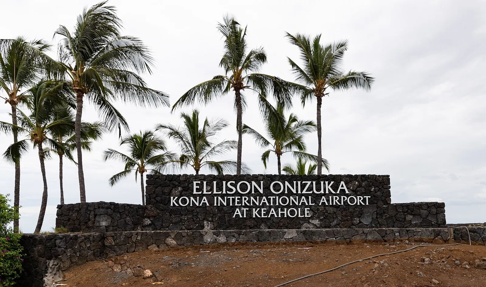 Lava-rock entrance sign for Ellison Onizuka Kona International Airport at Keahole, with coconut palms