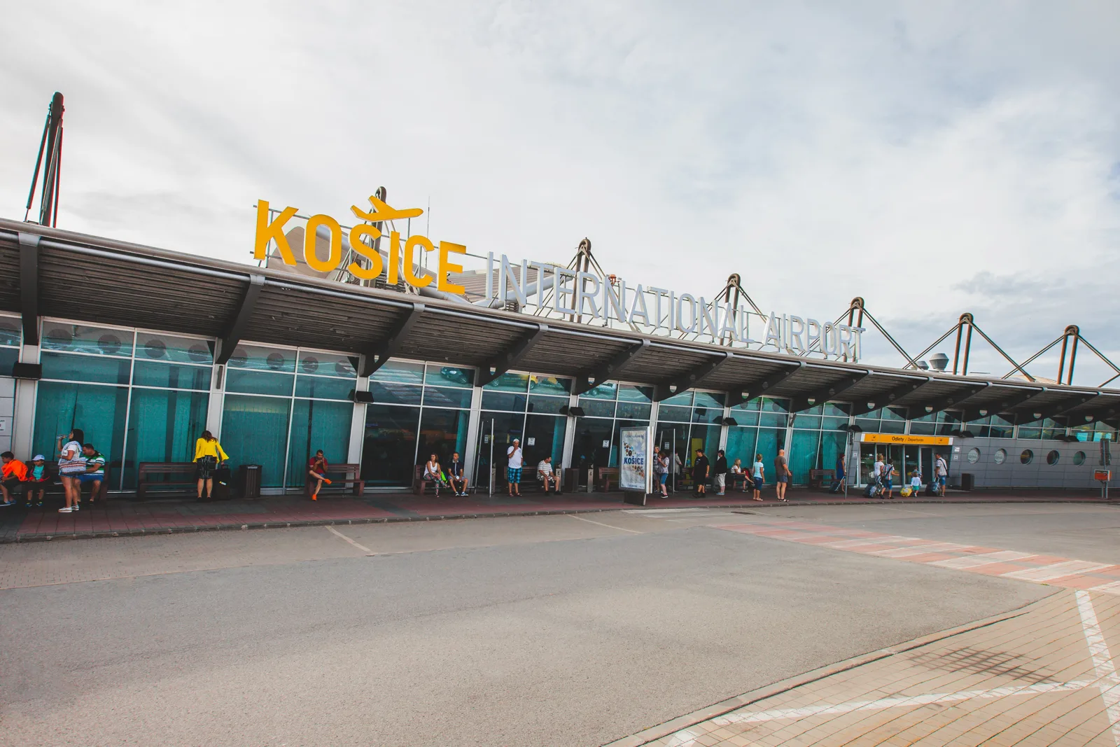 Front of the Košice International Airport terminal with the yellow KOŠICE INTERNATIONAL AIRPORT lettering on the canopy roof and a glass facade