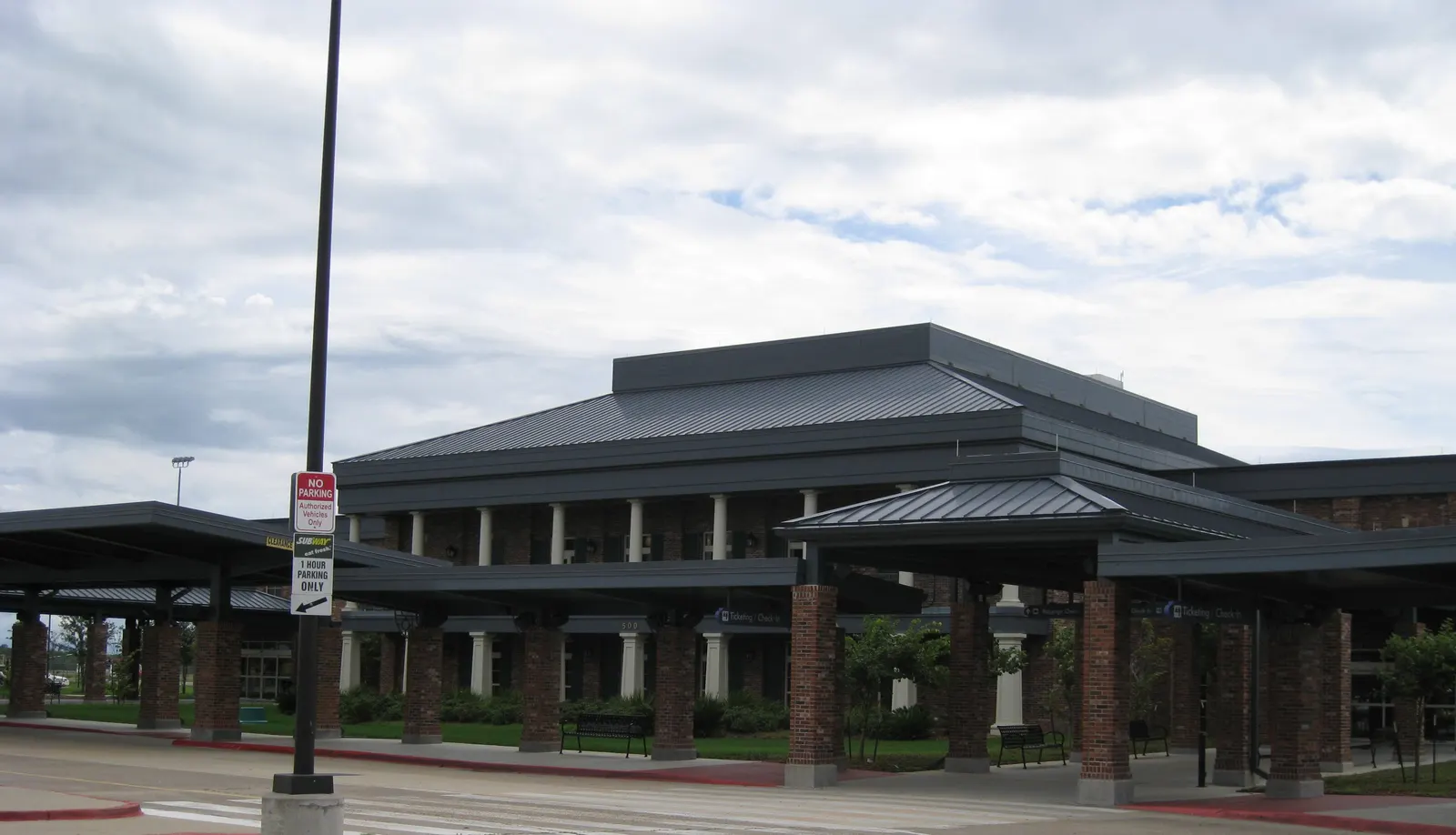 Brick-and-column porte-cochère of the Lake Charles Regional passenger terminal under a metal hip roof.