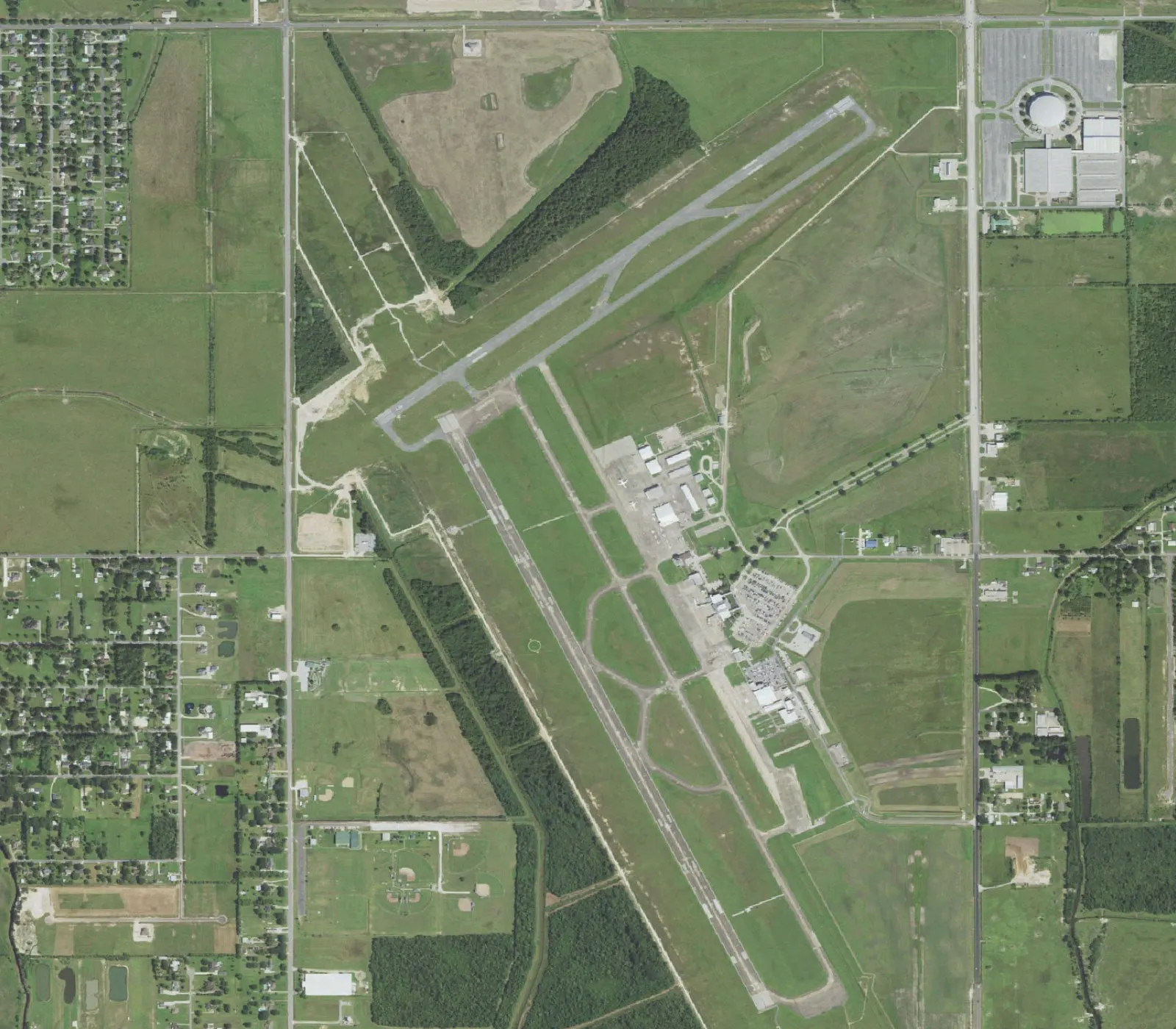 Overhead aerial of Lake Charles Regional Airport showing the uncrossed 15/33 and 5/23 runways, east-side terminal and parking lot, and the on-field NEXRAD dome.