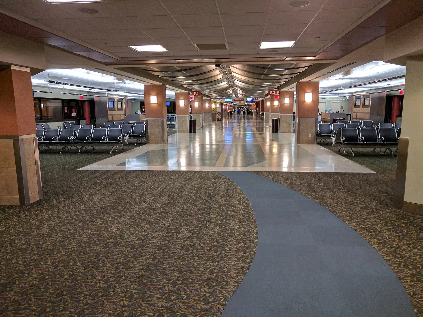 Empty Blue Grass Airport holdroom with a curved blue walkway and rows of black seats, photographed in September 2017.