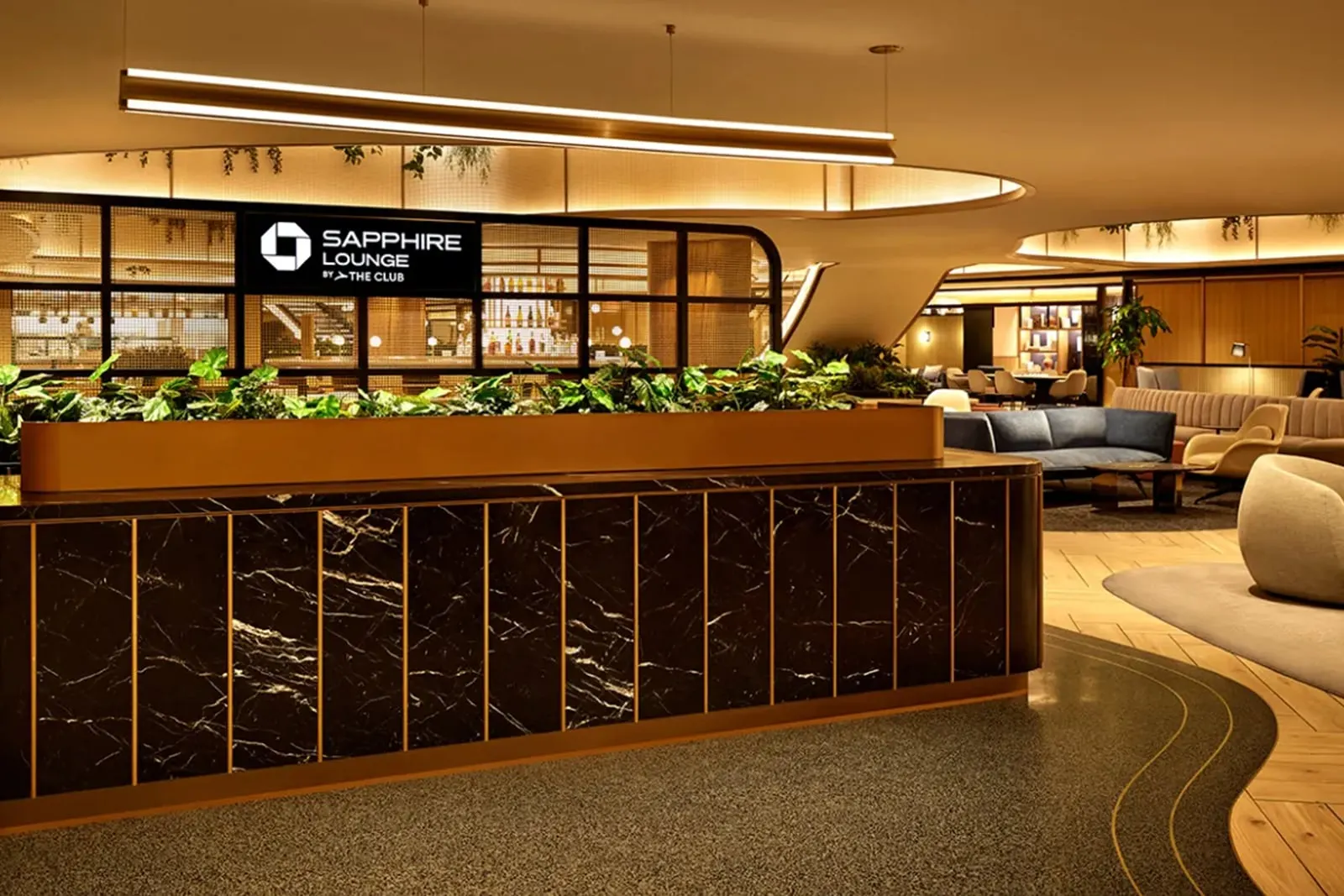 Curved black marble reception desk with living planter and Sapphire Lounge by The Club signage at the Chase Sapphire Lounge at LGA.