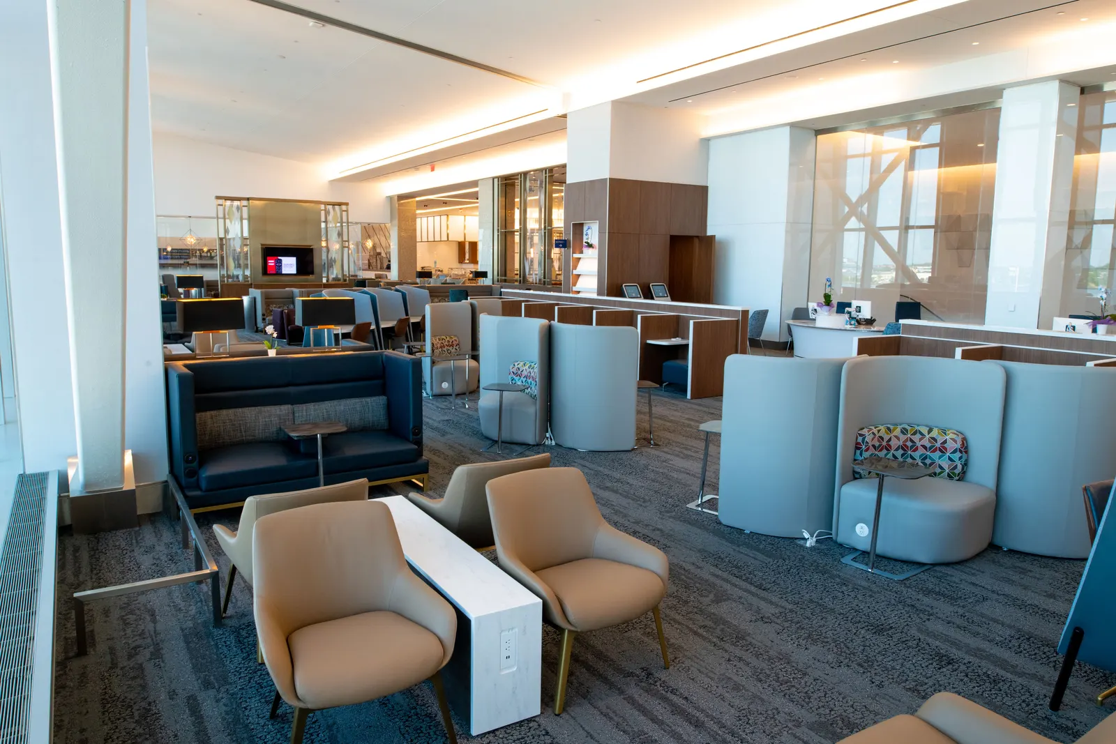 Tan chairs, blue booths and grey high-backs on patterned carpet facing wood media wall in the Delta Sky Club at LaGuardia (LGA).