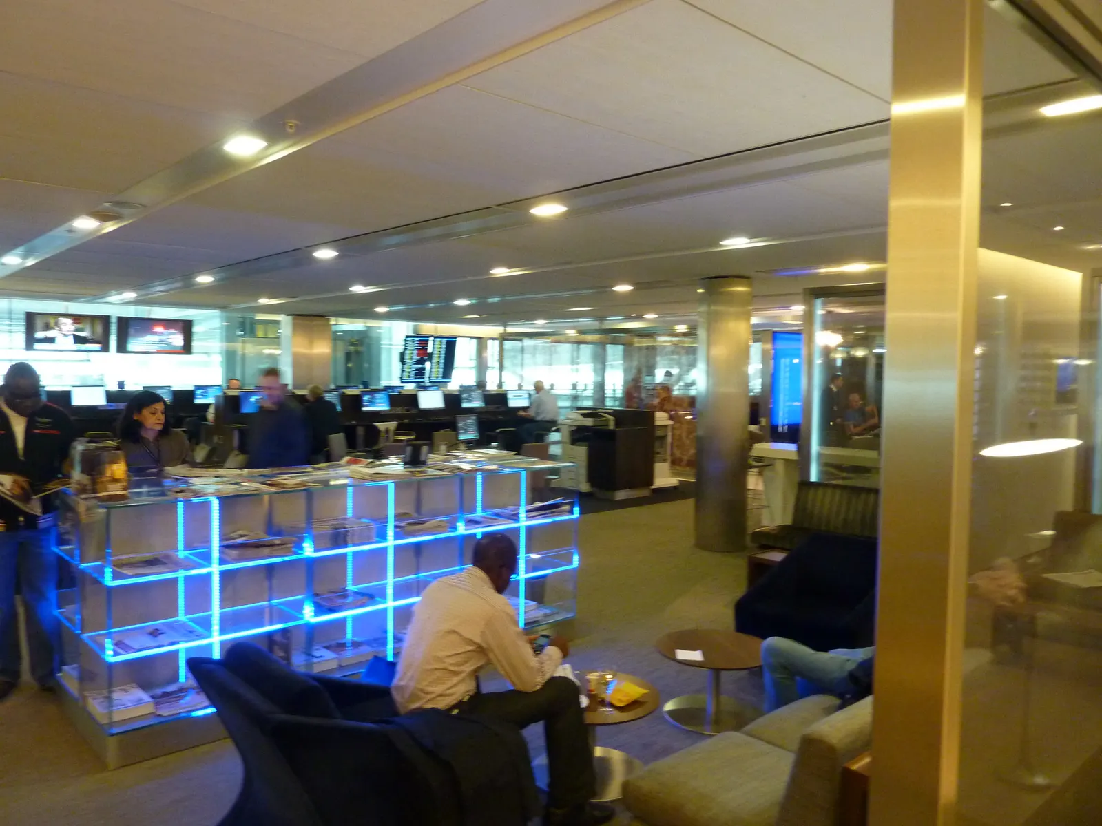 Blue LED magazine rack, armchair seating, and business-center workstations inside the British Airways Galleries Club Lounge at Heathrow Terminal 5 (LHR).