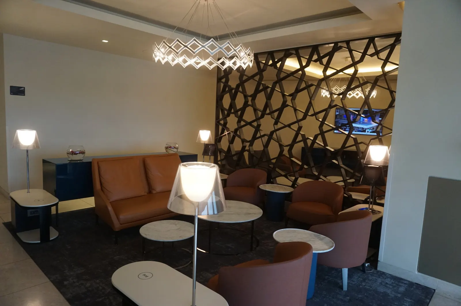 Tan leather seating, marble tables, and a lattice screen inside the Qatar Airways Premium Lounge at Heathrow Terminal 4 (LHR).
