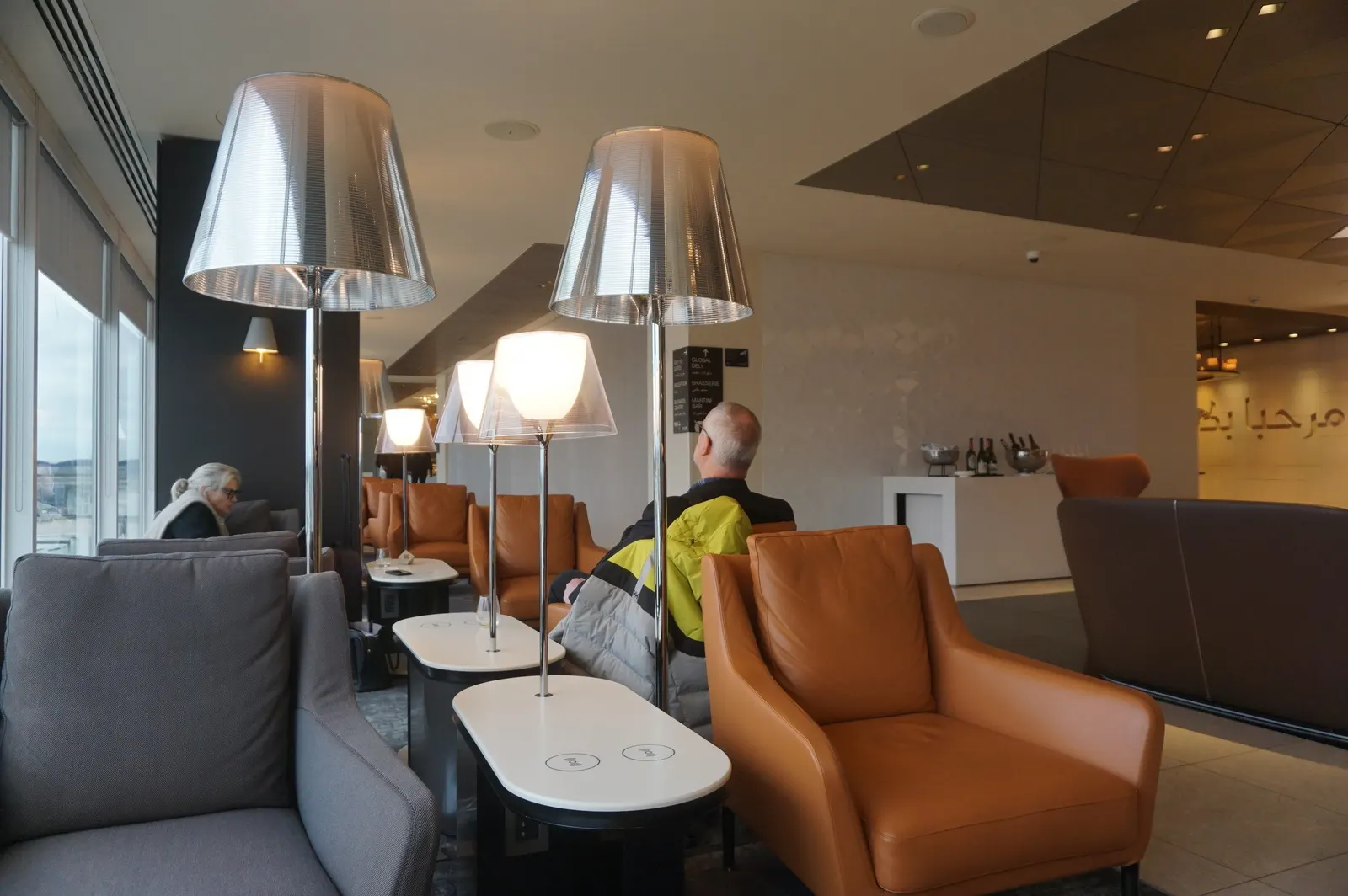 Armchairs with wireless-charging side tables facing the windows inside the Qatar Airways Premium Lounge at Heathrow Terminal 4 (LHR).