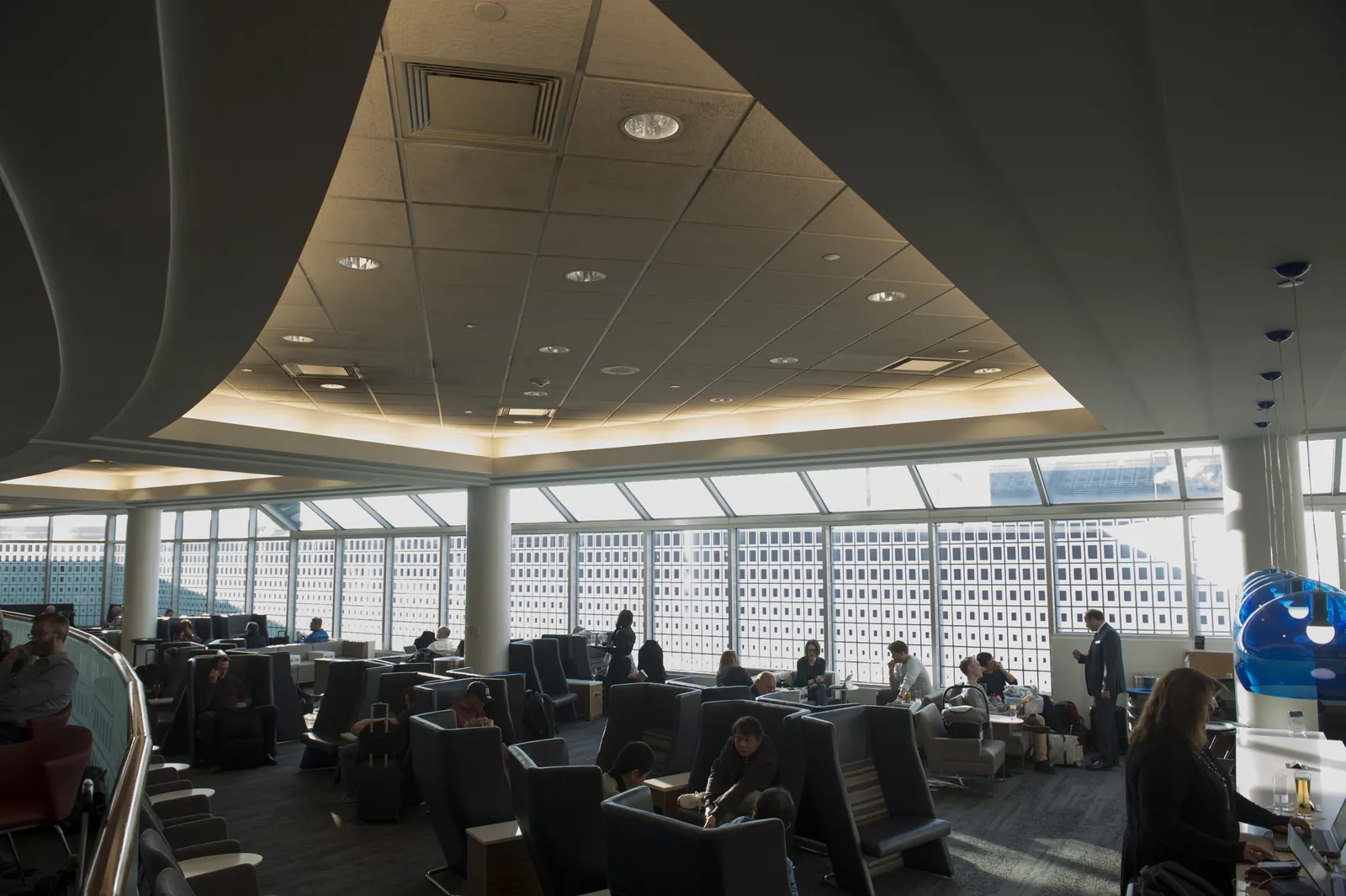 Rows of dark high-back privacy chairs facing slanted apron windows under a triangular lit ceiling cove inside the Delta Sky Club at Minneapolis-Saint Paul International Airport (MSP).