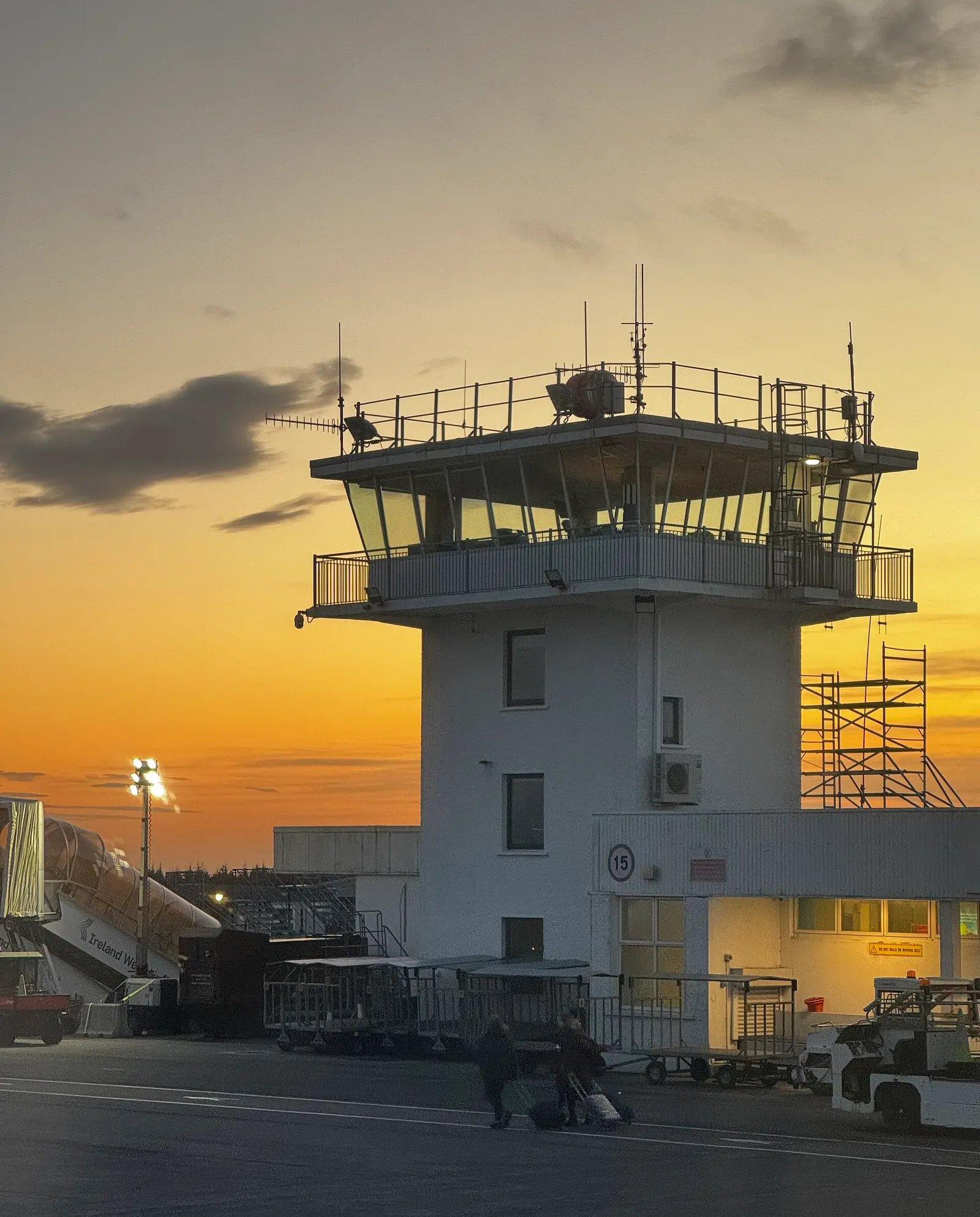 White control tower at Ireland West Airport Knock at sunset, with an Ireland West jet bridge and baggage carts on the apron.