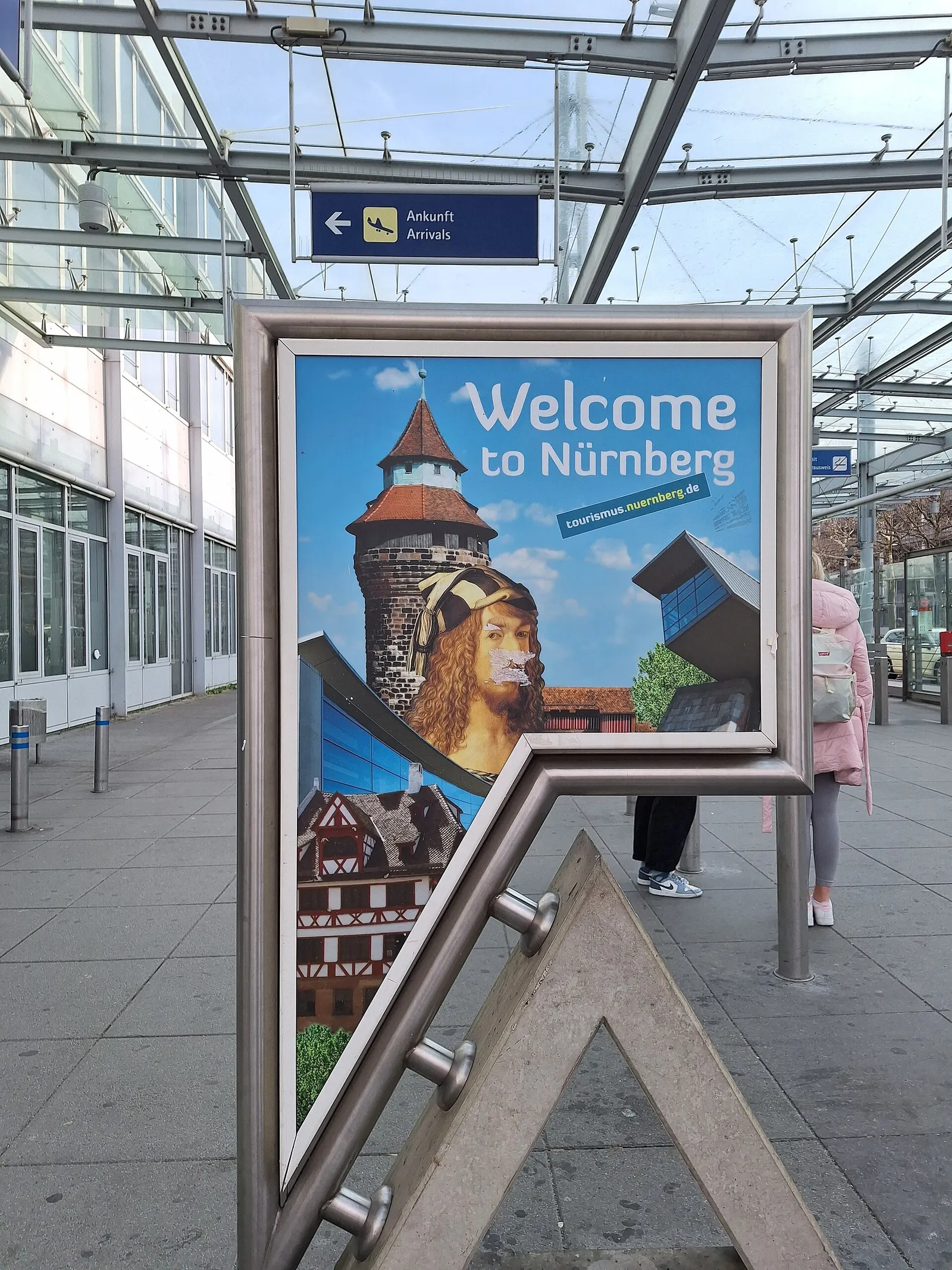 Welcome to Nürnberg poster under the glass arrivals canopy at Albrecht Dürer Airport, with an Ankunft / Arrivals sign overhead.