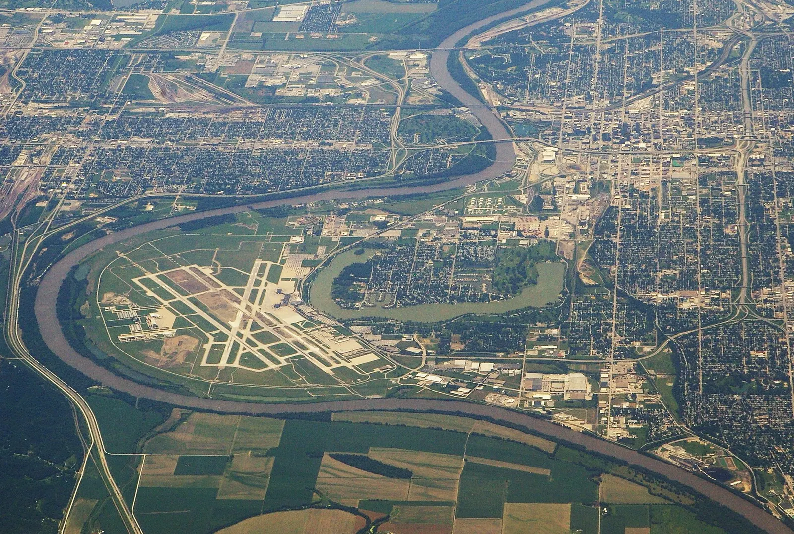 High-altitude aerial of Eppley Airfield’s three runways inside a Missouri River bend, with Carter Lake and the Omaha street grid to the west.