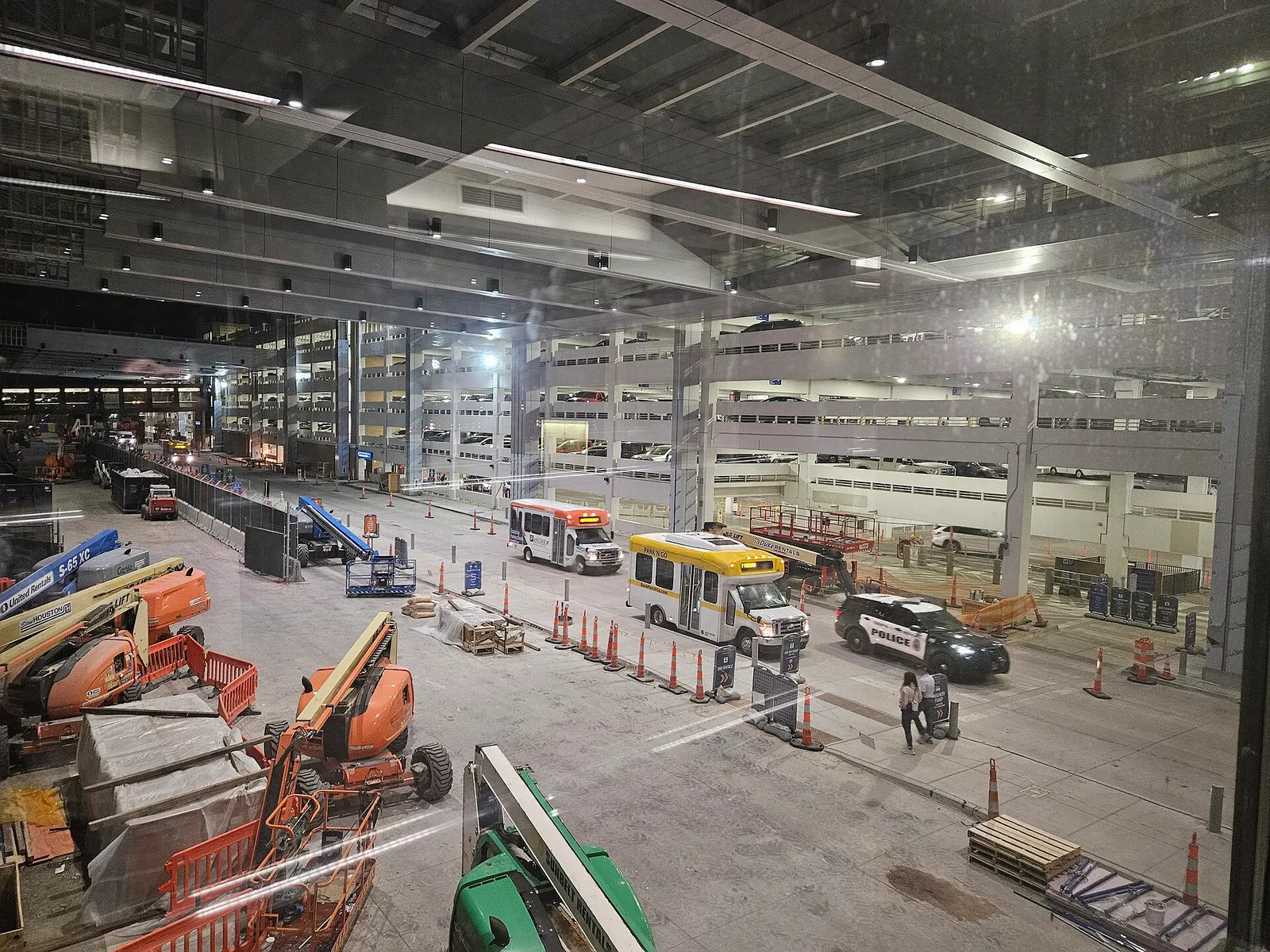 Night view from an Eppley skywalk of construction equipment, a Park N Go shuttle, an Omaha Airport Authority police SUV, and a multi-level parking garage.
