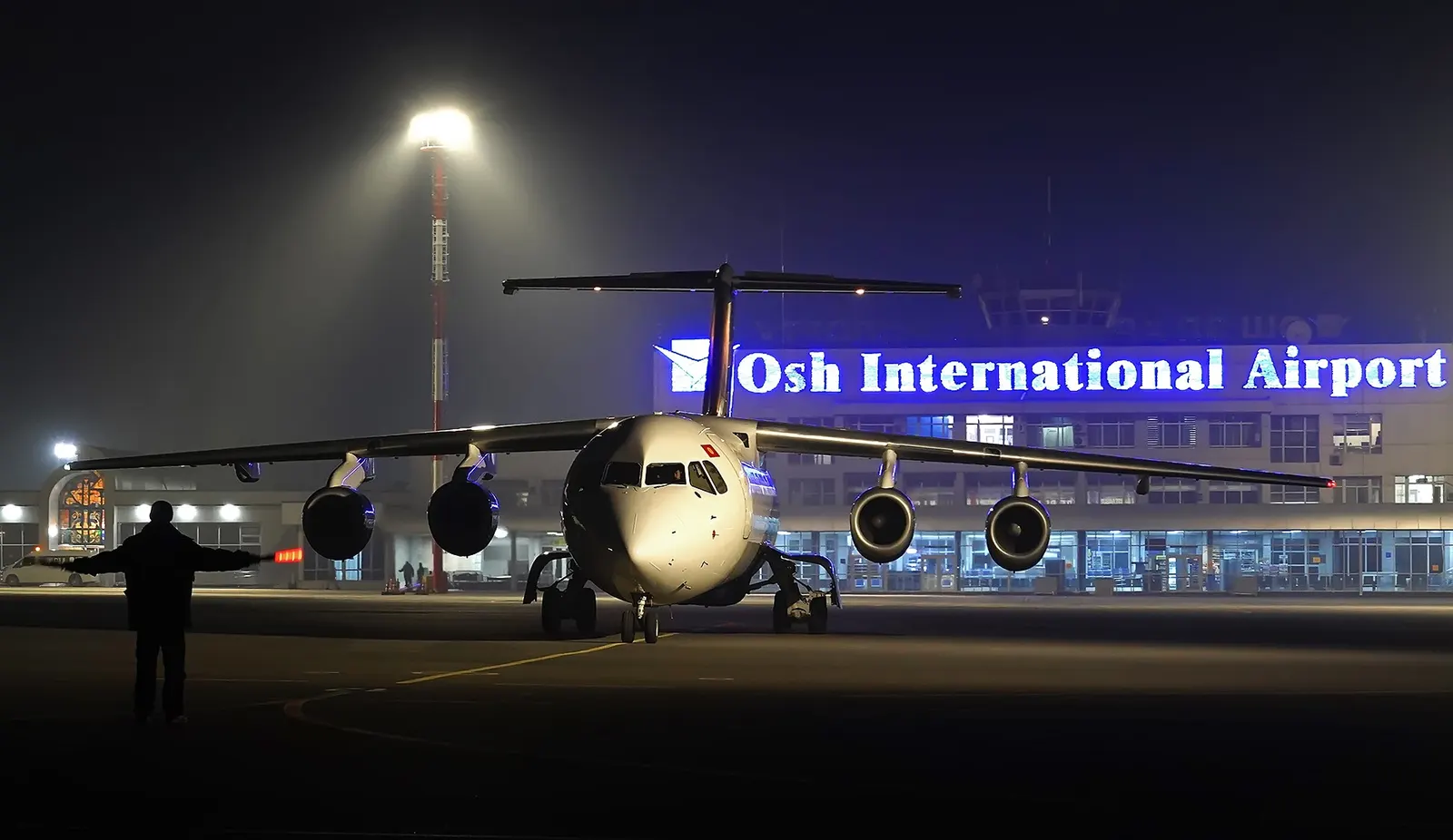 Osh Airport terminal at night with a TezJet aircraft on the apron