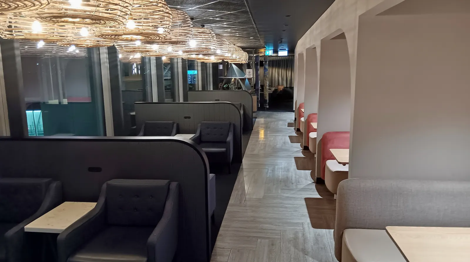 Private seating pods and grey lounge chairs under a row of woven circular pendant lights inside the International Aspire Lounge at Perth Airport (PER).