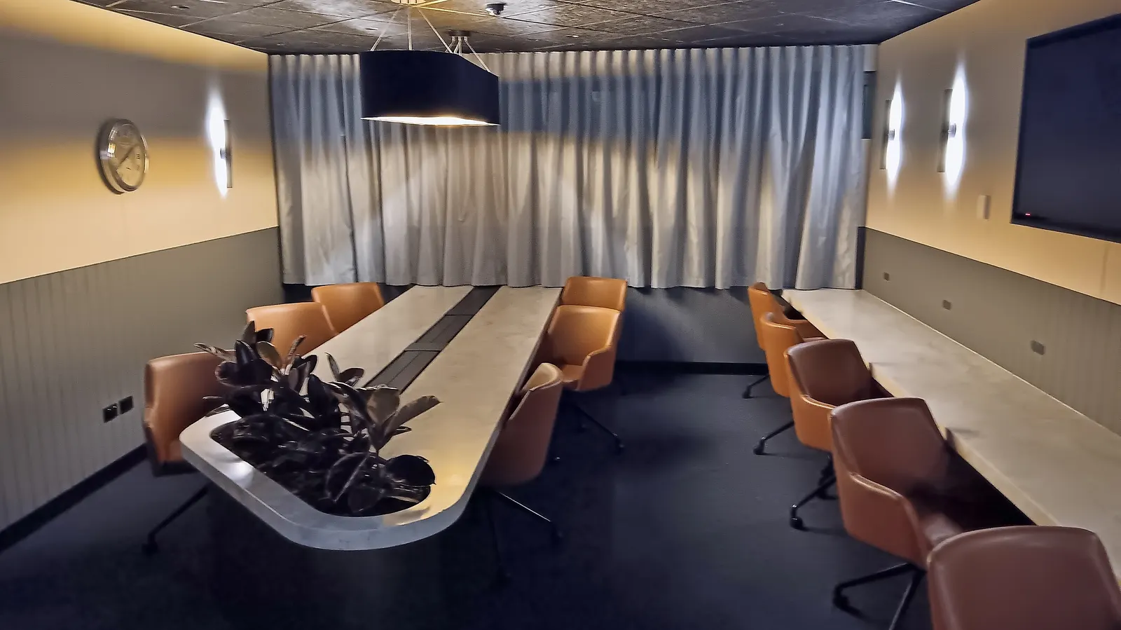 Business-center conference table with tan leather chairs, wall workstations, and warm sconces inside the International Aspire Lounge at Perth Airport (PER).