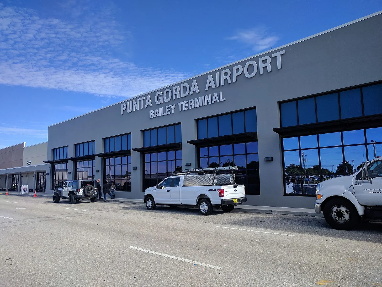 Gray Bailey Terminal facade at Punta Gorda Airport with PUNTA GORDA AIRPORT / BAILEY TERMINAL lettering and parked trucks at the curb.