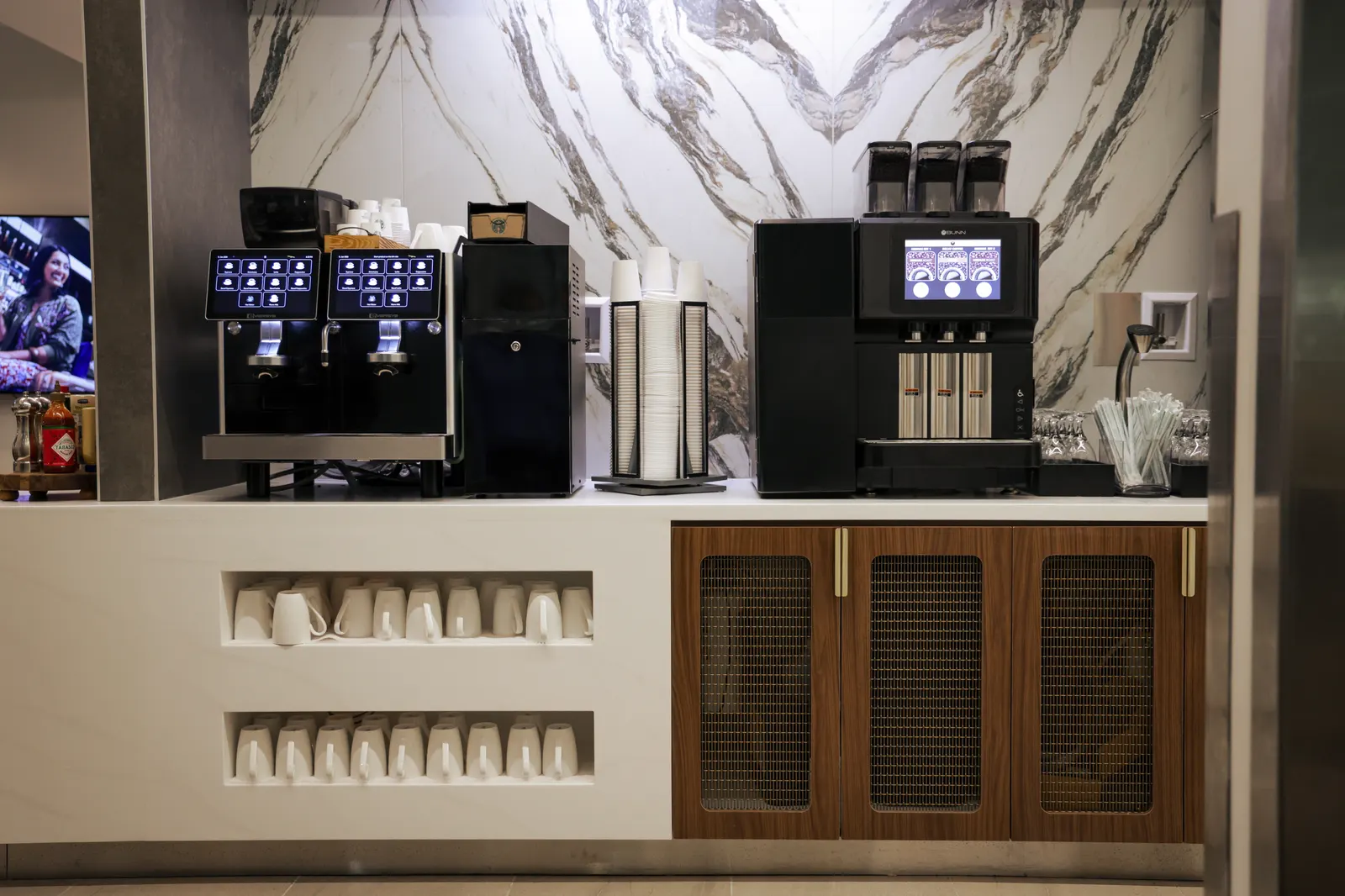 Self-serve espresso machines and mug shelves against marble panels in the renovated Delta Sky Club at Philadelphia (PHL).