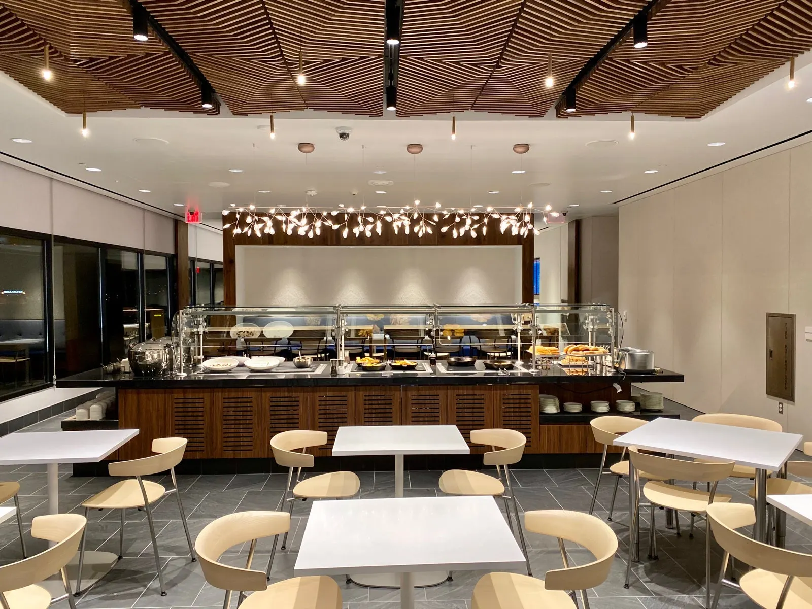 Buffet island and dining tables beneath a geometric wood-slat ceiling in The Centurion Lounge at Phoenix Sky Harbor (PHX).