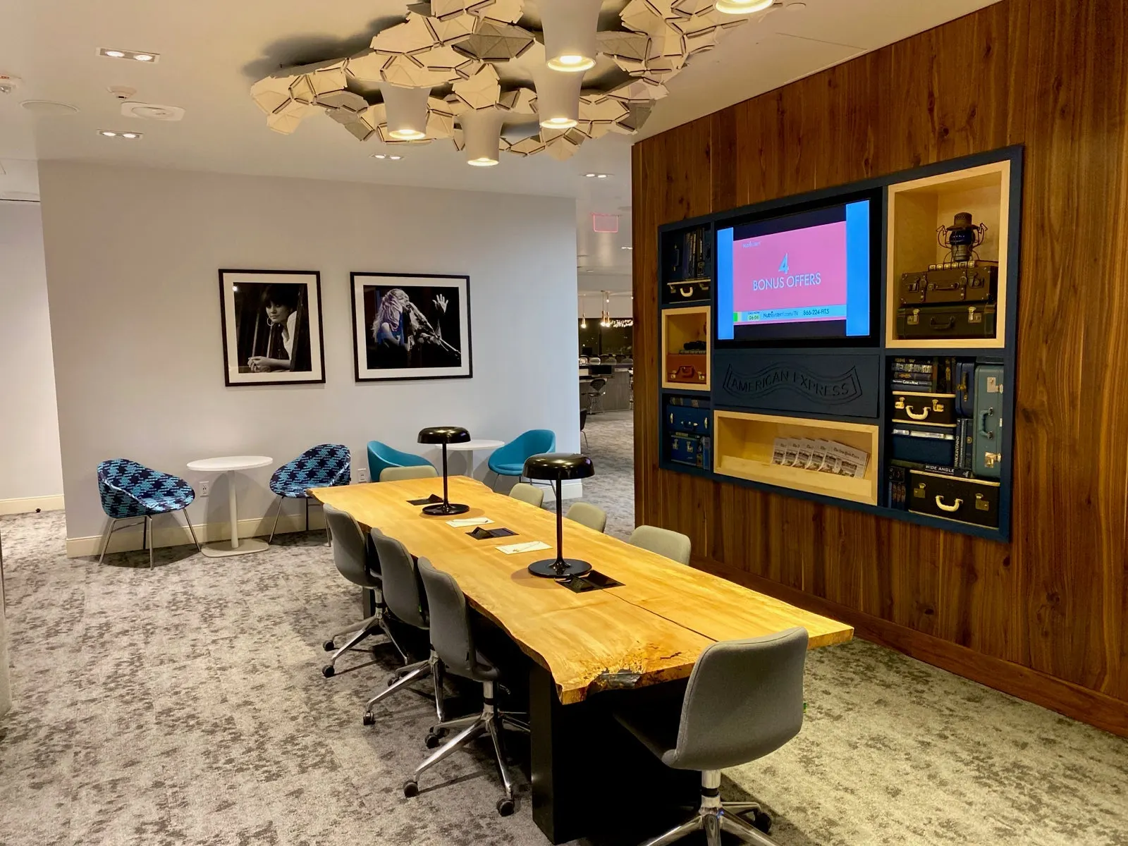 Communal wood work table and American Express media wall with vintage suitcase displays in The Centurion Lounge at Phoenix Sky Harbor (PHX).