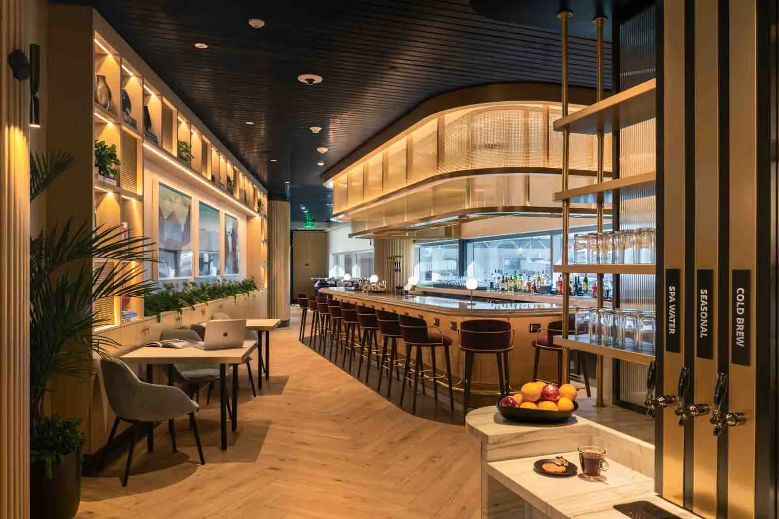 Marble servery with spa-water taps beside the curved bar and dining tables in the Chase Sapphire Lounge by The Club at Phoenix Sky Harbor (PHX).