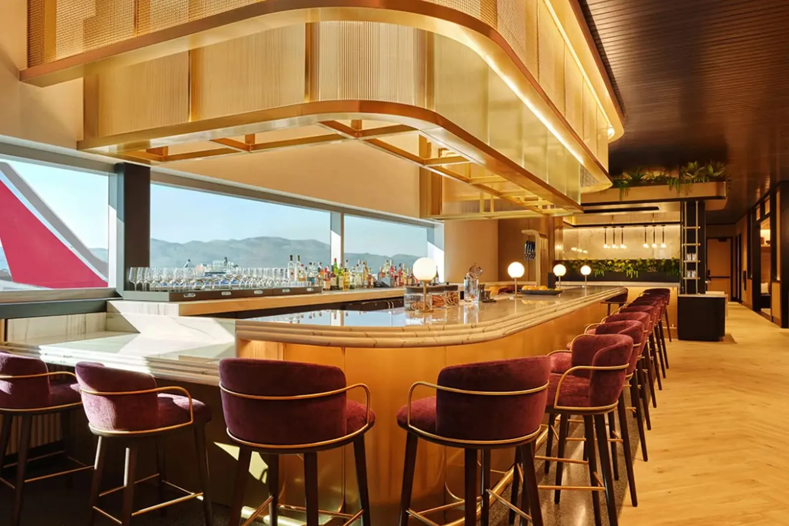 Gold-lit marble bar with plum stools overlooking the tarmac and desert mountains in the Chase Sapphire Lounge by The Club at Phoenix Sky Harbor (PHX).
