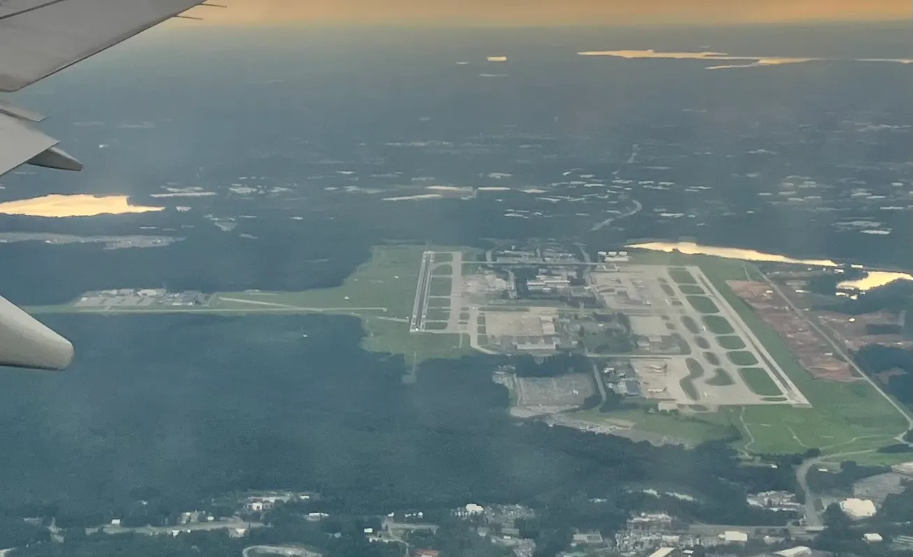 Aerial view of Raleigh-Durham International Airport showing both runways, the passenger terminals and surrounding lakes, photographed in July 2025.