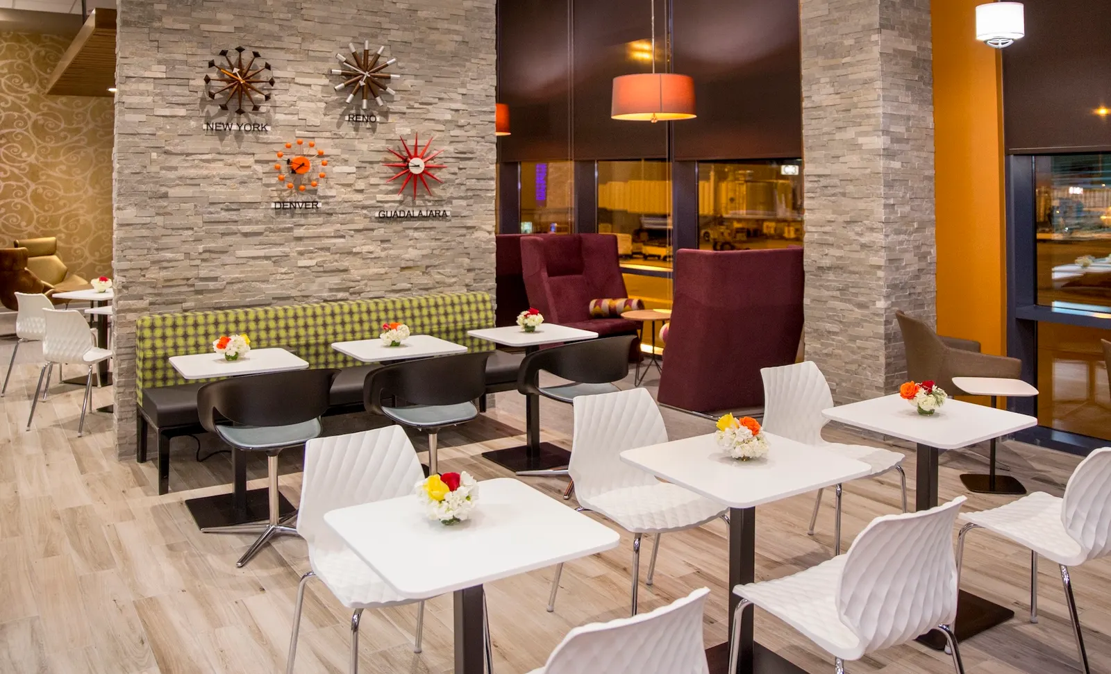 Dining tables and banquette seating under orange pendant lights in the Escape Lounge at Reno-Tahoe International Airport (RNO).