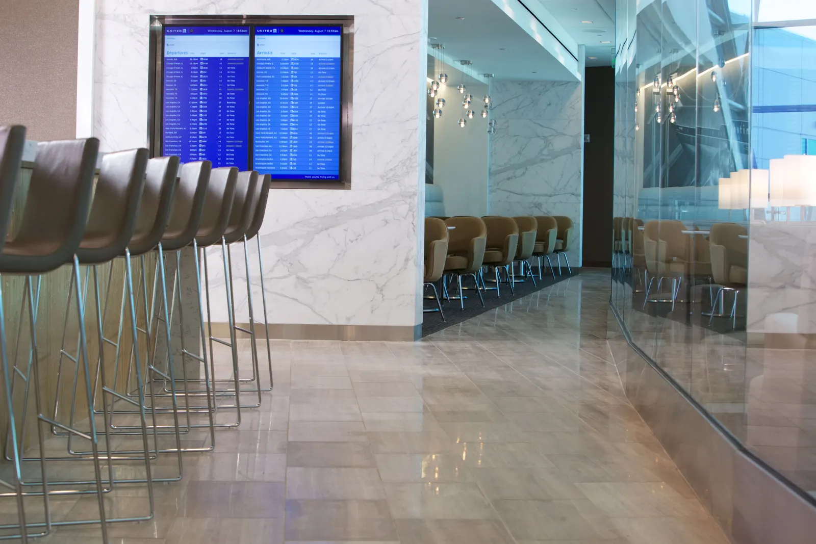 Barstools along a white marble corridor with flight displays in the United Club at San Diego (SAN).