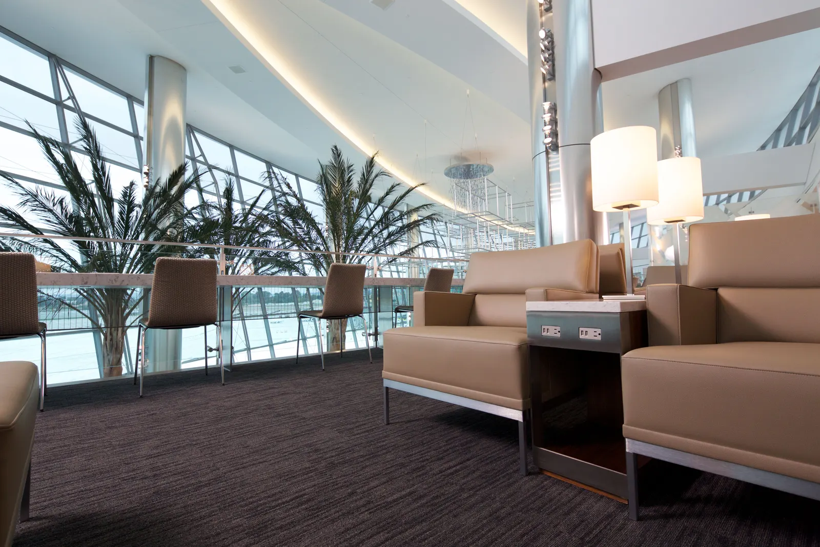 Tan armchairs and work counter with palm trees beside slanted airfield windows in the United Club at San Diego (SAN).