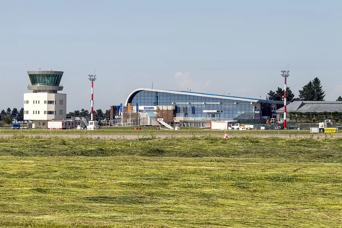 Glass-fronted passenger terminal with a SOSIRI (arrivals) sign and the white control tower at Suceava airport, seen across the grass beside the runway