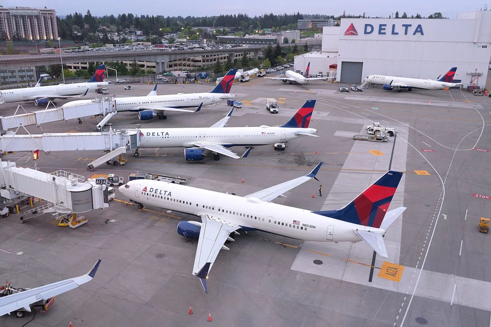 Delta Air Lines Boeing 737-900ER N853DN parked at gate A12A at Seattle-Tacoma International Airport, as well as other aircraft parked behind it, as seen from the S concourse pedestrian bridge