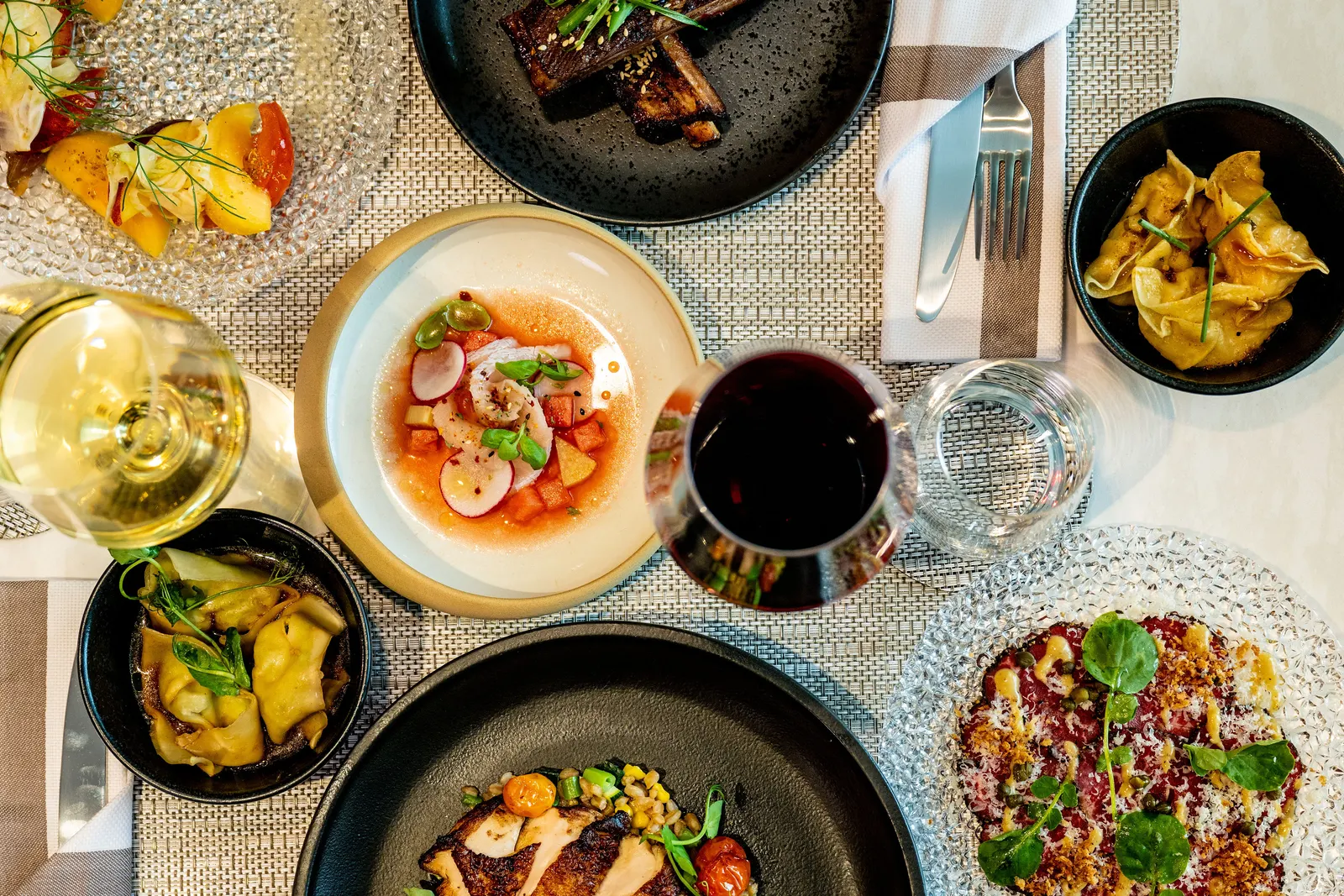 Plated multi-course dishes with wine glasses on a textured placemat in the Delta One Lounge at Seattle-Tacoma (SEA).