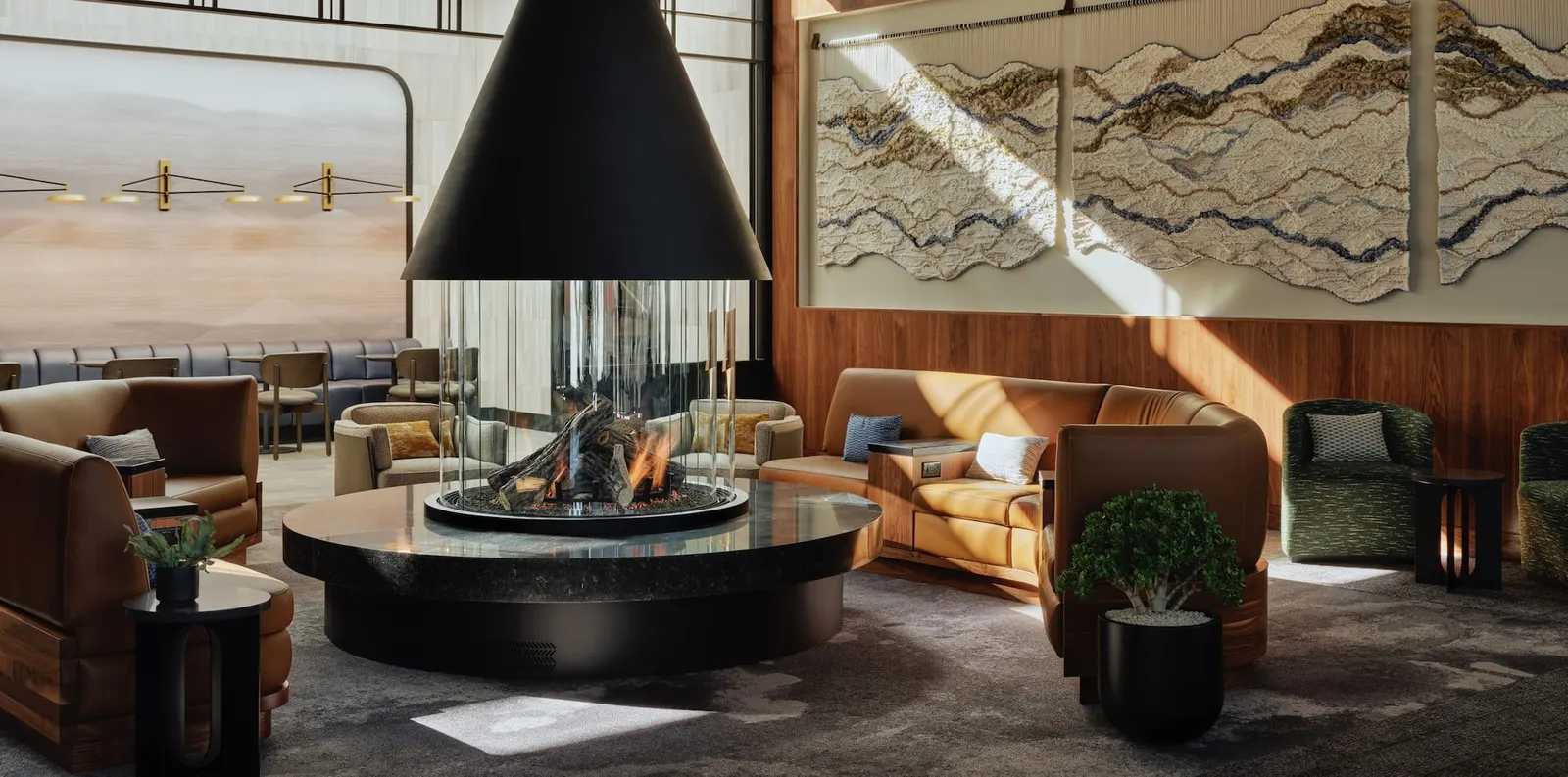 Circular glass hearth with tan leather banquettes and mountain-inspired wall art in The Centurion Lounge at Salt Lake City (SLC).