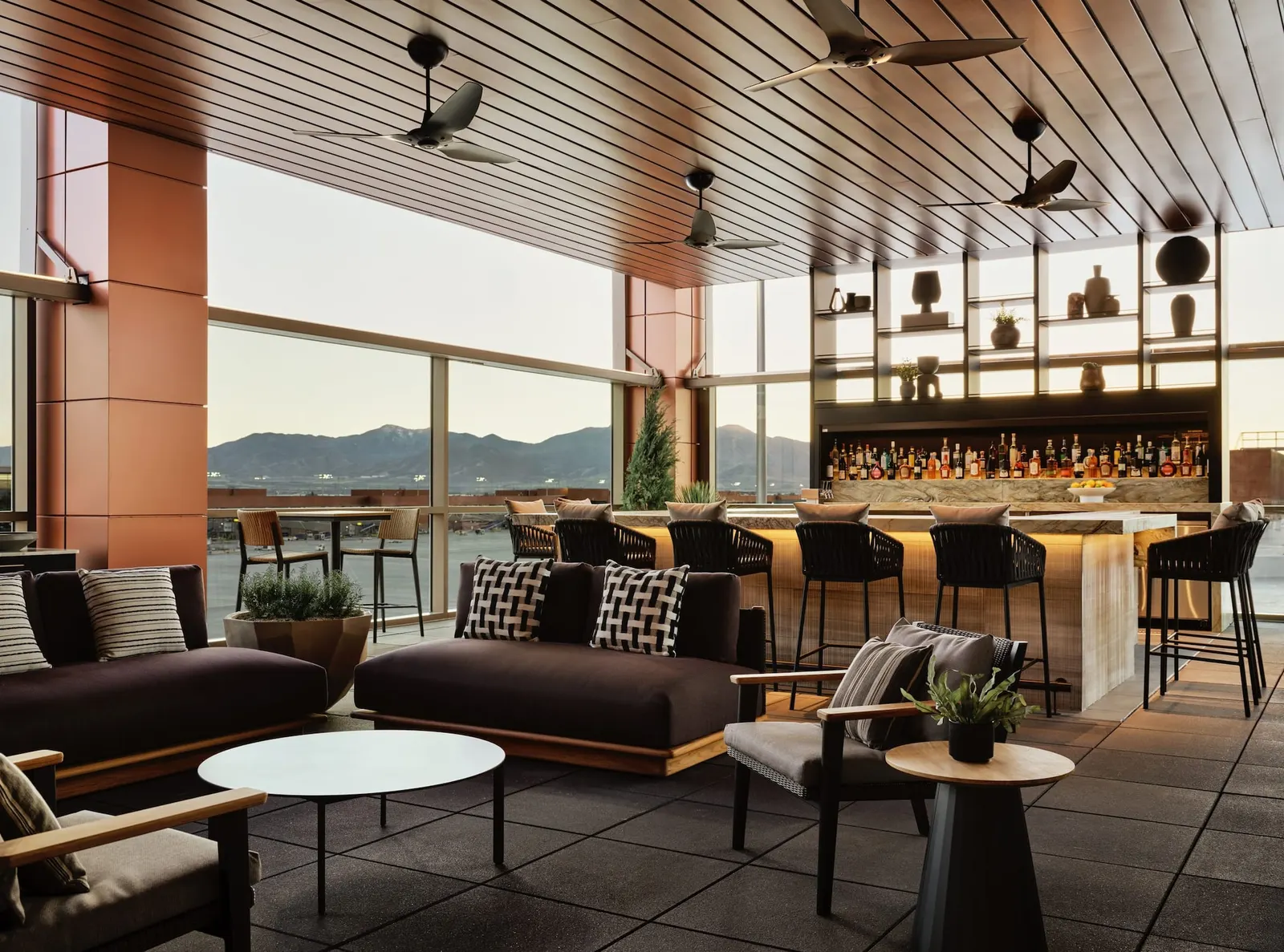 Lounge seating and backlit bar with mountain views through floor-to-ceiling windows in The Centurion Lounge at Salt Lake City (SLC).