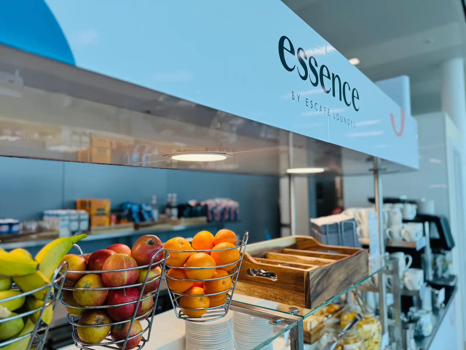Fruit and bread buffet under Essence by Escape Lounges signage at London Stansted Airport (STN).