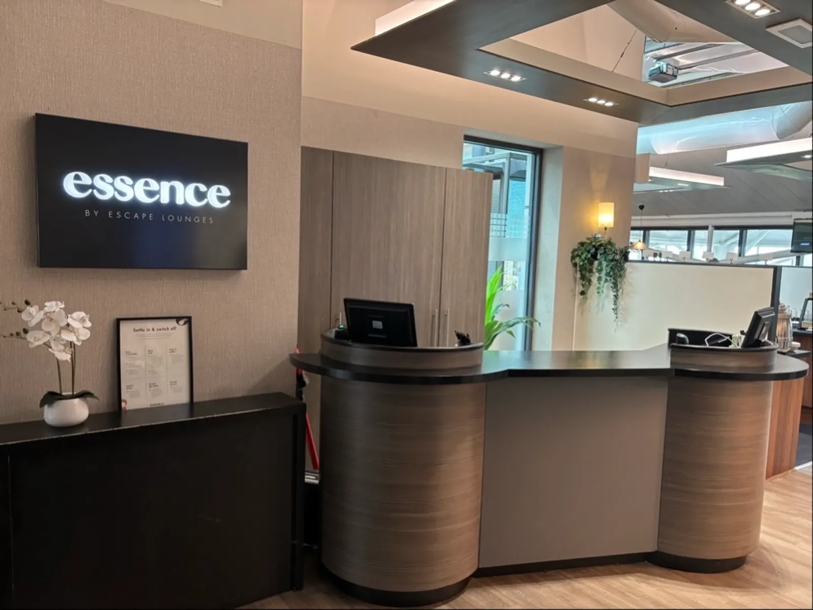 Wood reception desk and Essence by Escape Lounges illuminated sign at London Stansted Airport (STN).