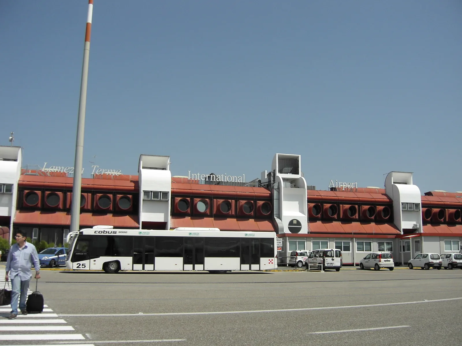 Lamezia Terme Airport passenger terminal seen across the forecourt, with red-and-white facade towers and a bus on the forecourt road, August 2010