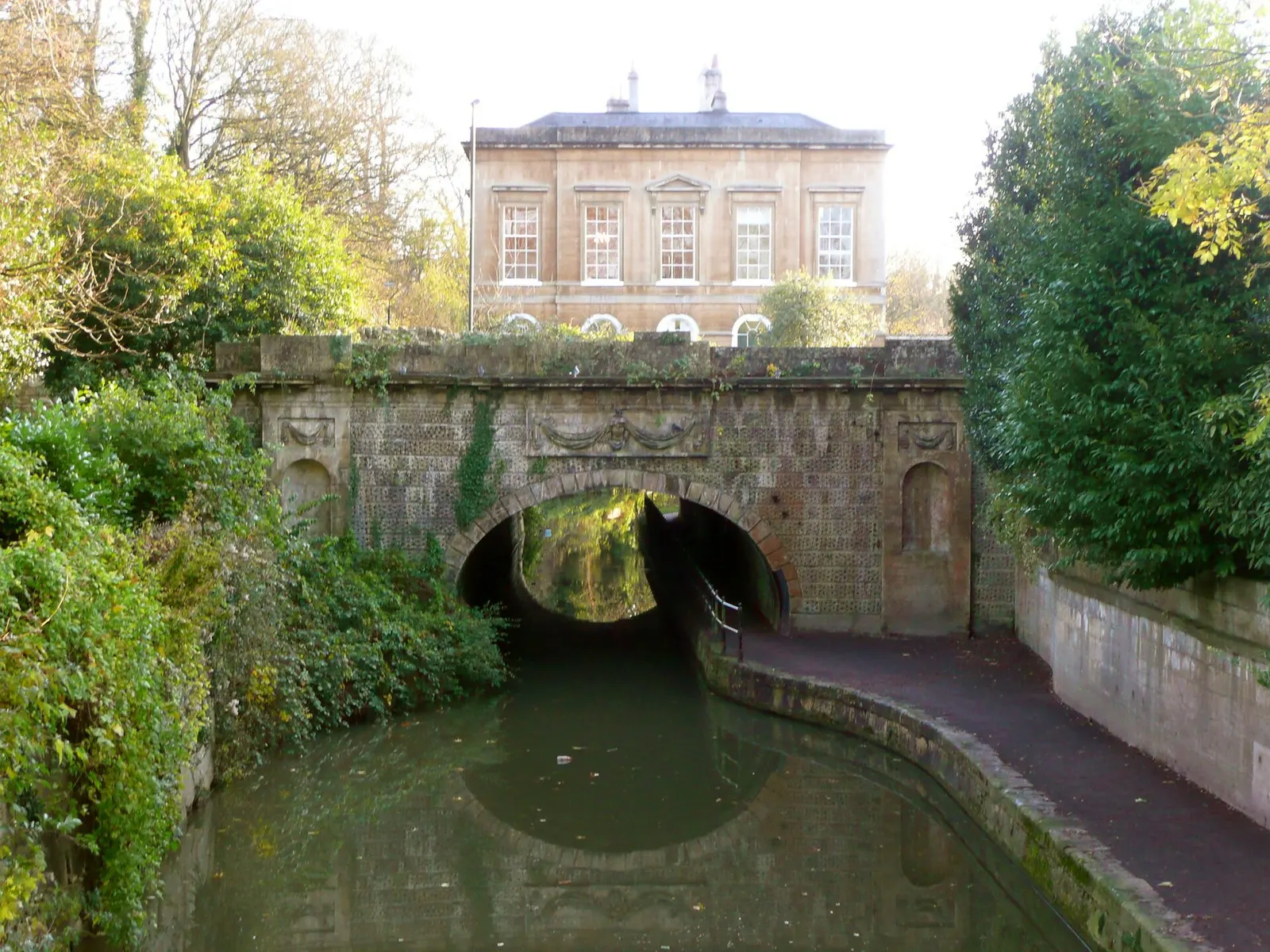 Which came first? The canal was constructed through Sydney Gardens between 1800 and 1810, and Pevsner describes Cleveland House, which is over the tunnel, as being early 19C. I should think that the canal was made in a cutting and covered over, with a tunnel portal at each end, and the house built o