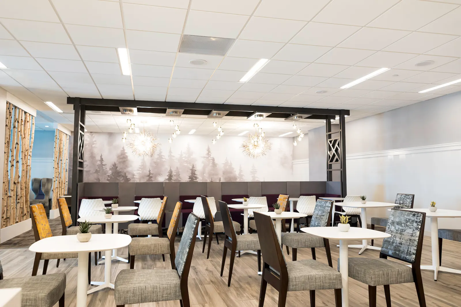 Dining tables, patterned chairs and forest mural banquette in the Escape Lounge at Syracuse Hancock International Airport (SYR).