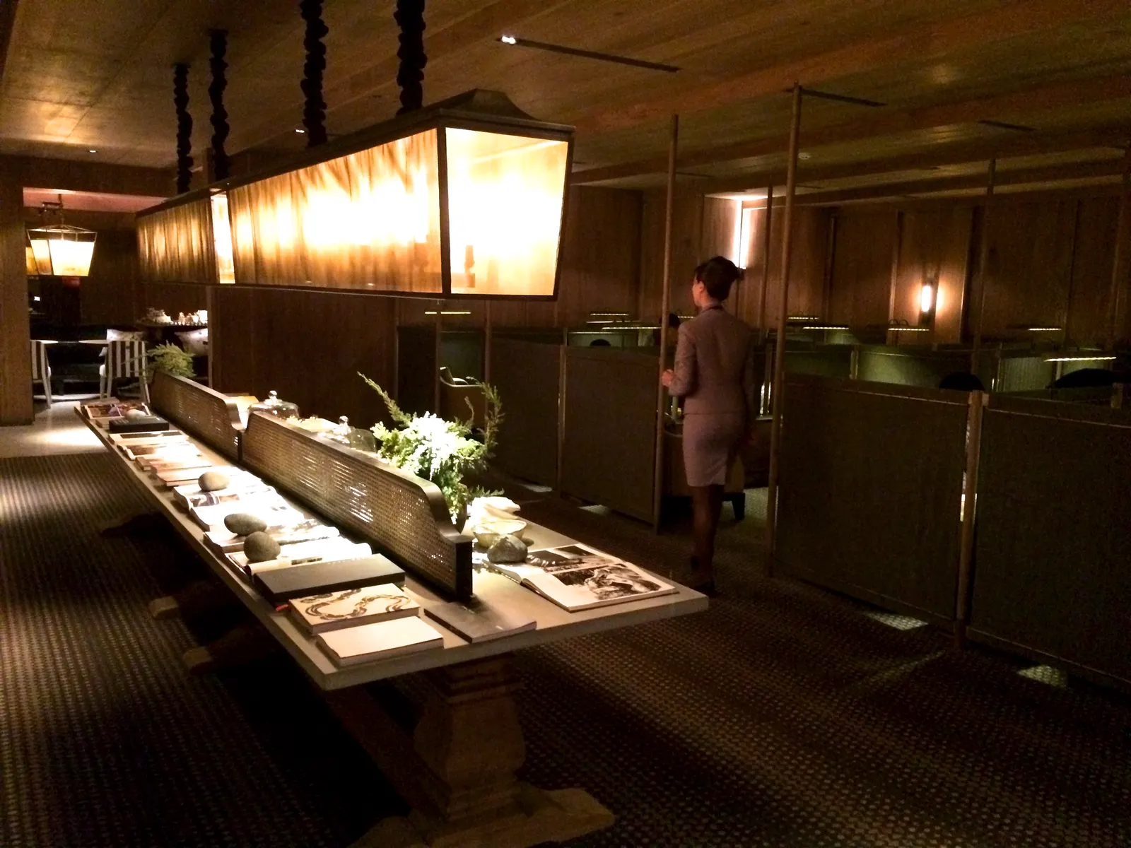 Long wood communal table under a translucent box light with booth seating beyond inside the China Airlines Dynasty Lounge First Class section at Taiwan Taoyuan International Airport (TPE).
