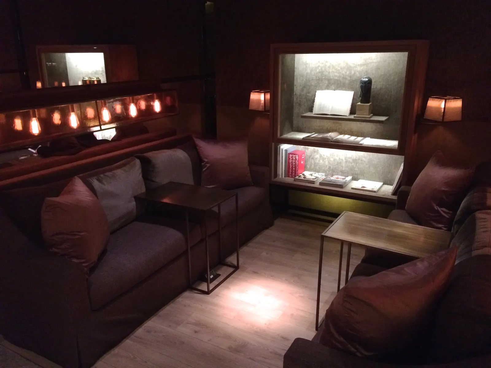 Charcoal sofa with cushions beside lit wall shelves and hanging bulbs inside the China Airlines Dynasty Lounge Business Class section at Taiwan Taoyuan International Airport (TPE).
