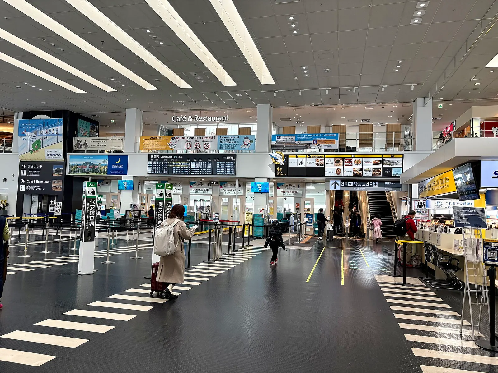 Bright Terminal 1 departure hall at Kobe Airport with check-in counters, self-service kiosks, and a high glass ceiling.