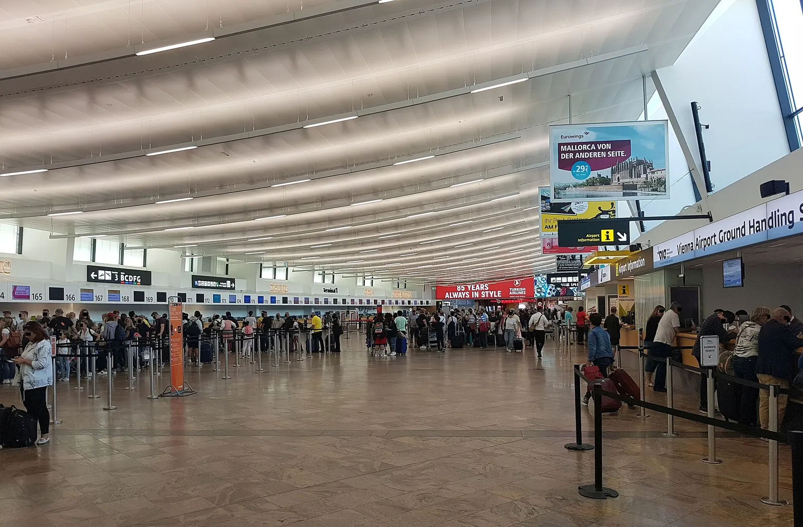 Busy Terminal 1 check-in hall at Vienna Airport with stanchioned queues and Vienna Airport Ground Handling desks.