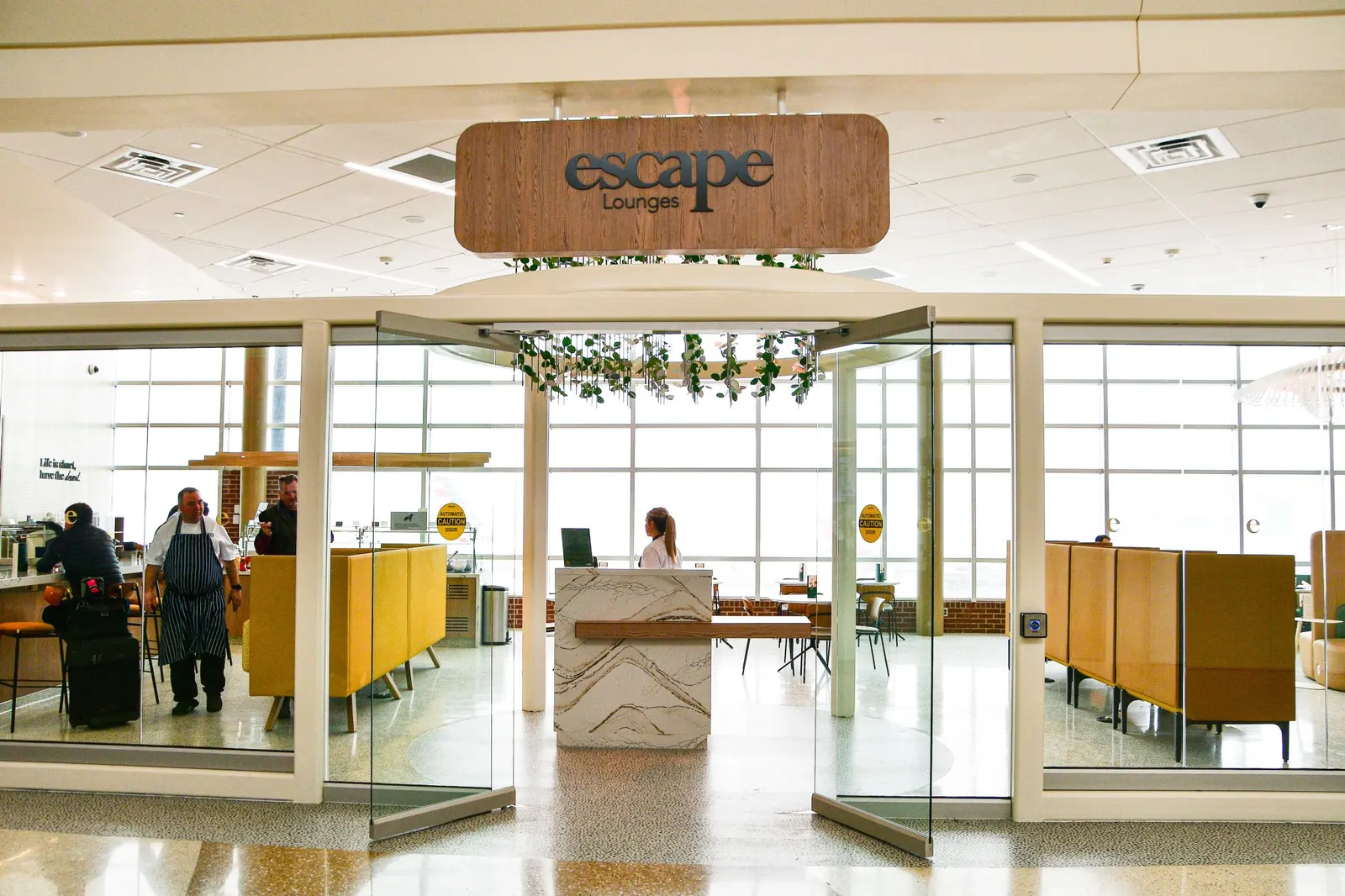 Glass entrance and reception desk of the Escape Lounge at Northwest Arkansas National Airport (XNA).