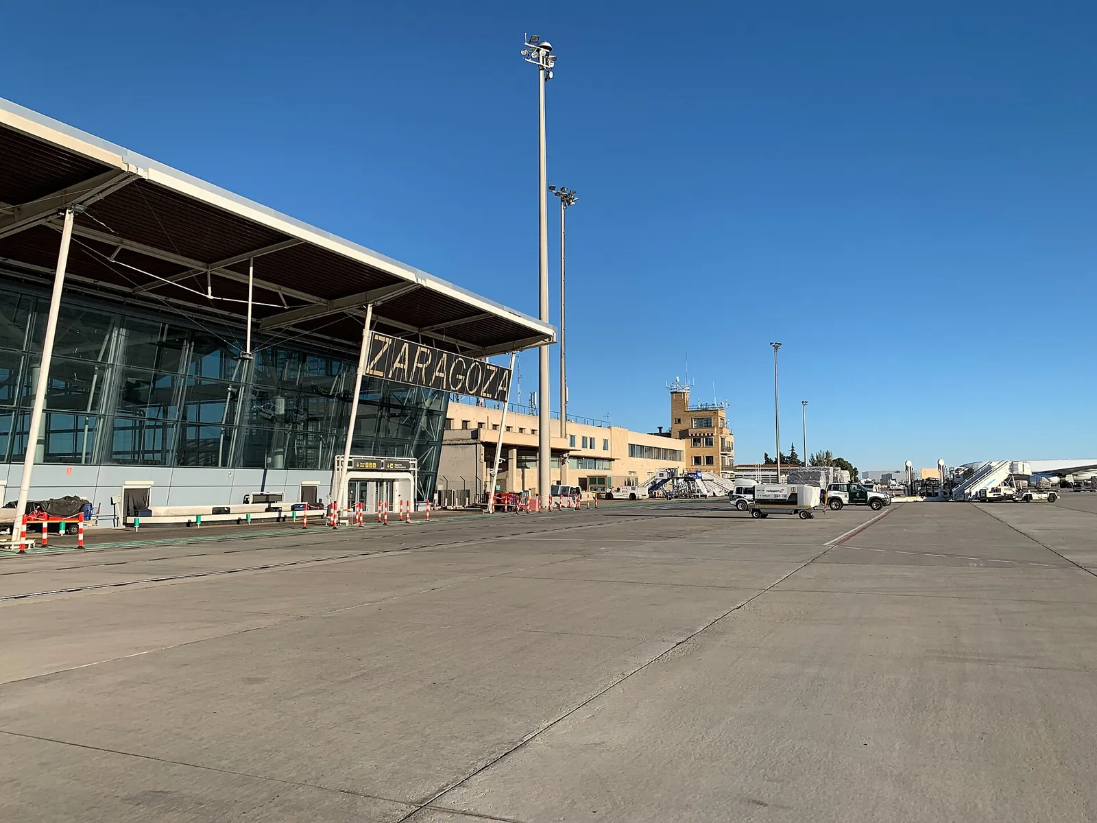 Glass and steel Zaragoza terminal seen from the apron under a clear blue sky, with its wave-shaped roof edge and the airport name on the facade